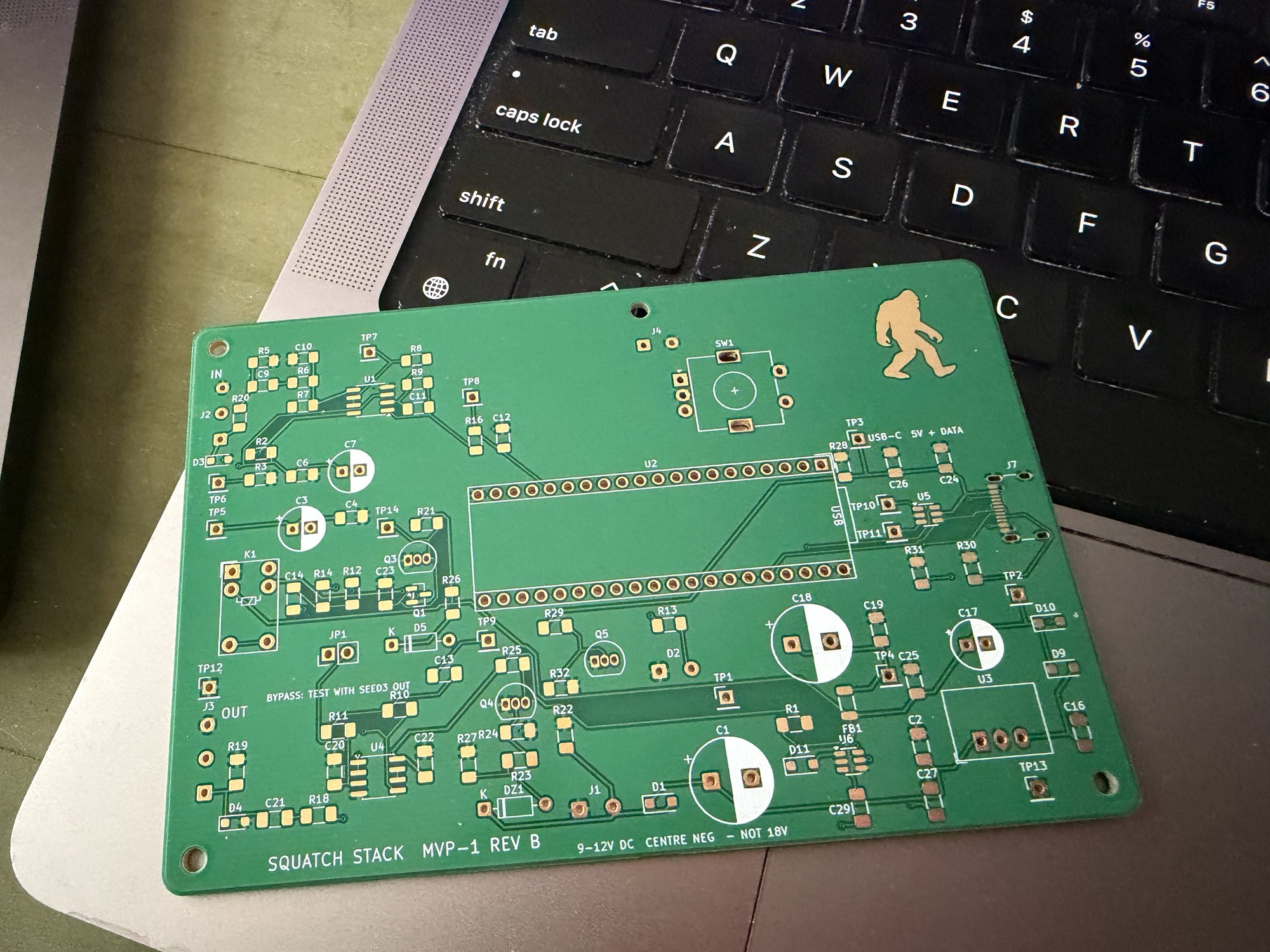 A green MVP-1 Rev B circuit board with a gold Squatch mark, bare and unassembled, resting on a laptop keyboard